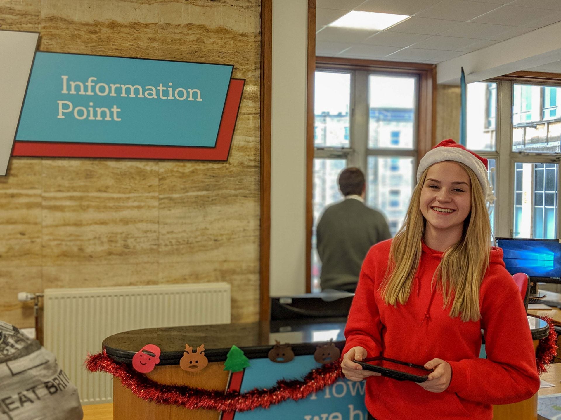 Olivia stands in front of the Information Point desk with an iPad in her hands
